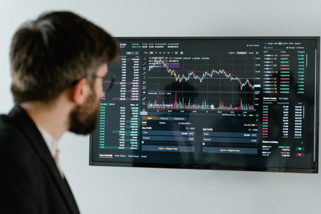 Automatyzacja inwestowania: Mężczyzna w garniturze obserwuje wykresy giełdowe na ekranie monitora, symbolizując połączenie ludzkiej decyzji i technologicznej analizy.