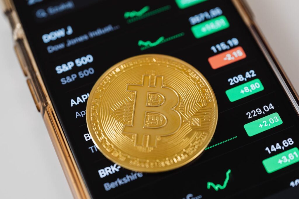Symbol Bitcoina na tle aplikacji giełdowej na smartfonie, obrazujący wpływ technologii blockchain na finanse i bankowość.