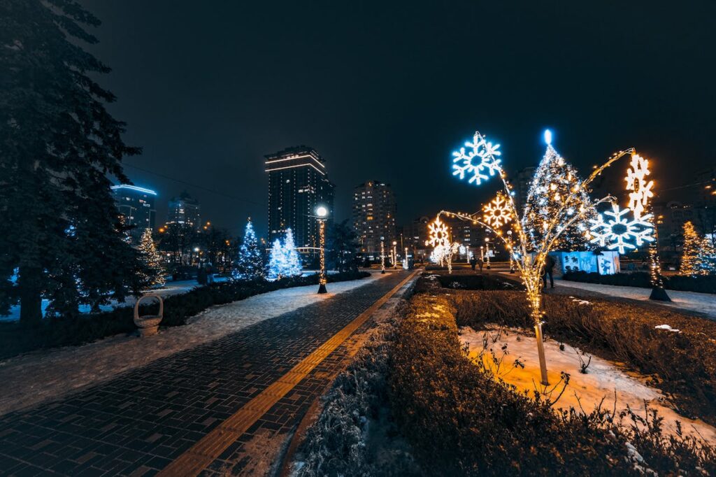 Między sacrum a neonem: estetyka świątecznych iluminacji w polskich miastach – nocny widok miejskiego parku ozdobionego świątecznymi światłami, z podświetlonymi choinkami i świetlnymi płatkami śniegu na tle nowoczesnych budynków.