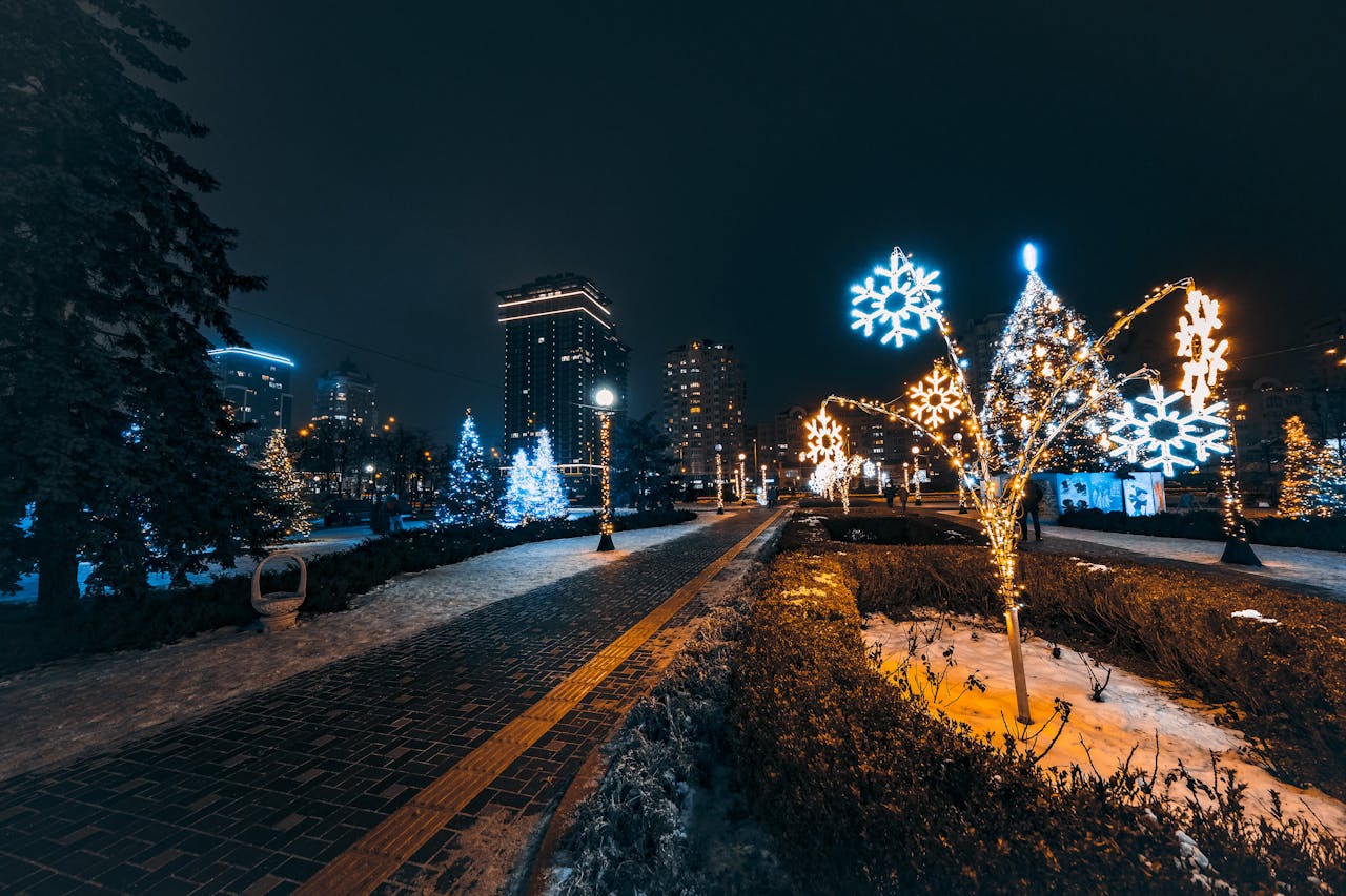 Między sacrum a neonem: estetyka świątecznych iluminacji w polskich miastach – nocny widok miejskiego parku ozdobionego świątecznymi światłami, z podświetlonymi choinkami i świetlnymi płatkami śniegu na tle nowoczesnych budynków.