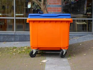 Pomarańczowy plastikowy kontener na odpady poremontowe i śmieci stojący przed budynkiem